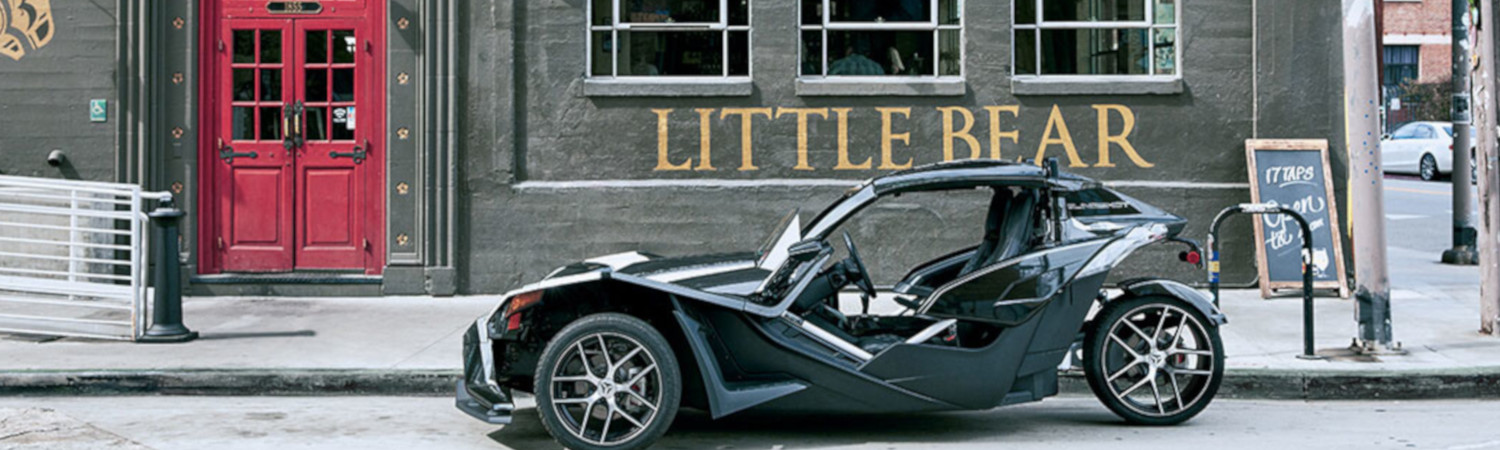 Black Polaris Slingshot Grand Touring motorcycle next to a building.